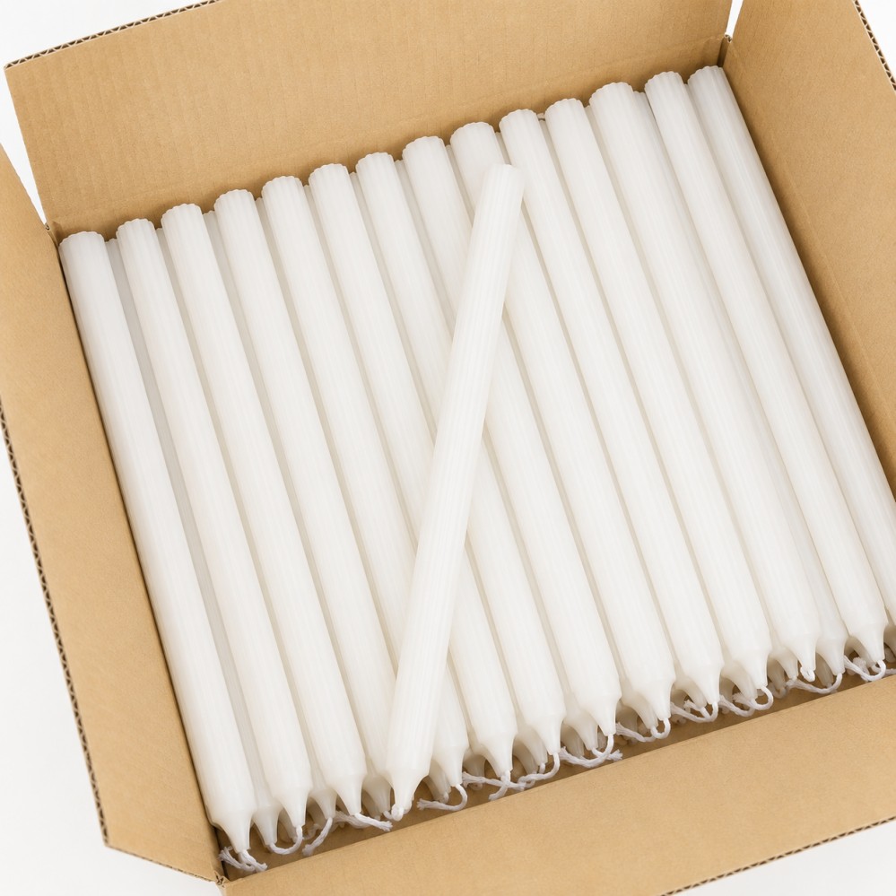 Open carton filled with white fluted taper candles arranged neatly for wholesale supply
