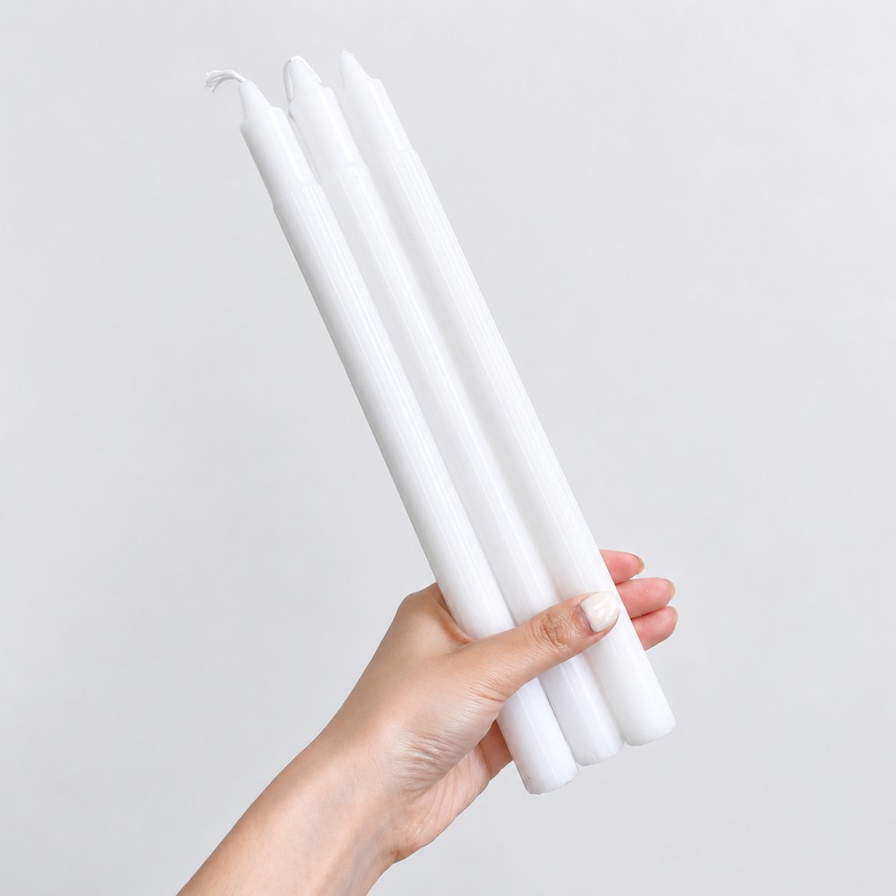 white fluted taper candle with ribbed texture in front of a box of long dinner candles